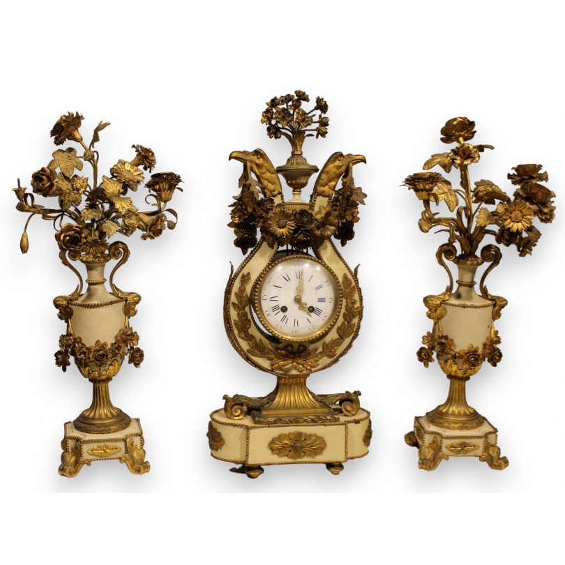 A clock and two candlesticks made of beige and bronze-coloured sheet metal