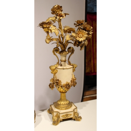 A clock and two candlesticks made of beige and bronze-coloured sheet metal